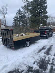 A truck and trailer loaded with logs and tree debris in a snowy driveway, handled by Mr. Groundhog Disposal and Services in Bloomington, MN.
