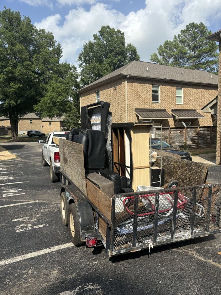 A white pickup truck with a utility trailer loaded with furniture and other junk, being hauled by MOAT's Junk Removal LLC in Jonesboro, AR.