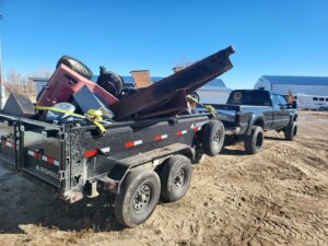 A pickup truck pulling a dump trailer loaded with heavy metal and construction debris by Rubble Removers LLC in Riverton, WY.