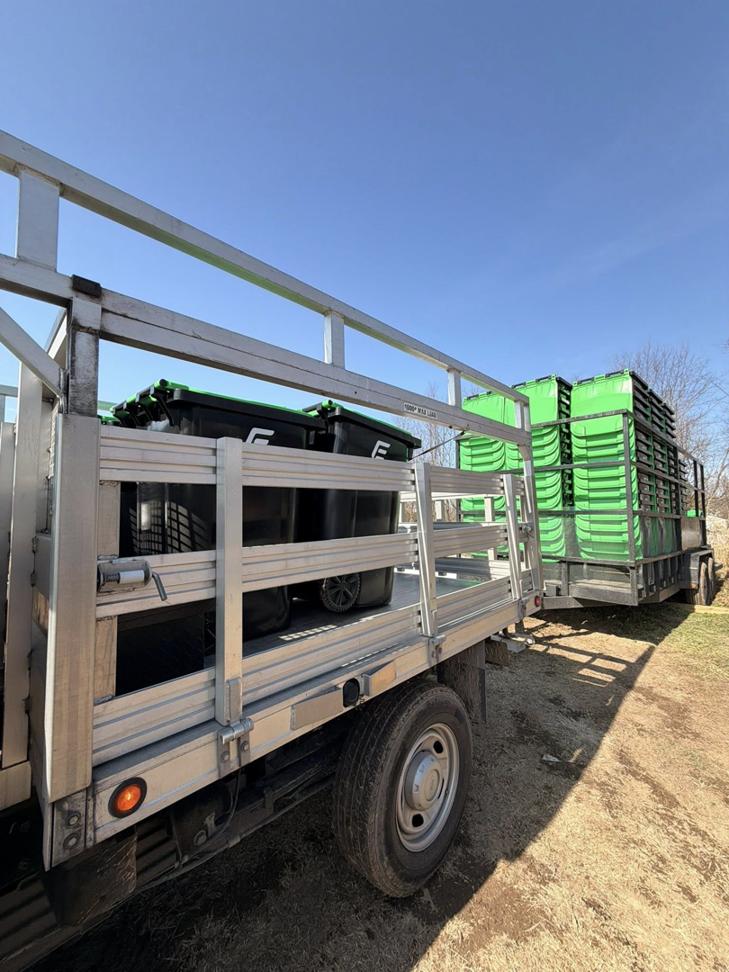A truck and trailer loaded with green and black disposal bins for Elevate Disposal Services, LLC in Bentonville, AR