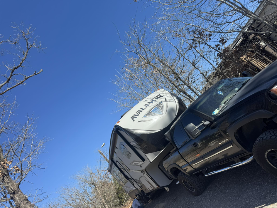 A black pickup truck transporting a white Avalanche fifth-wheel RV for Trash Junkies & Transport Services in Thornville, OH.