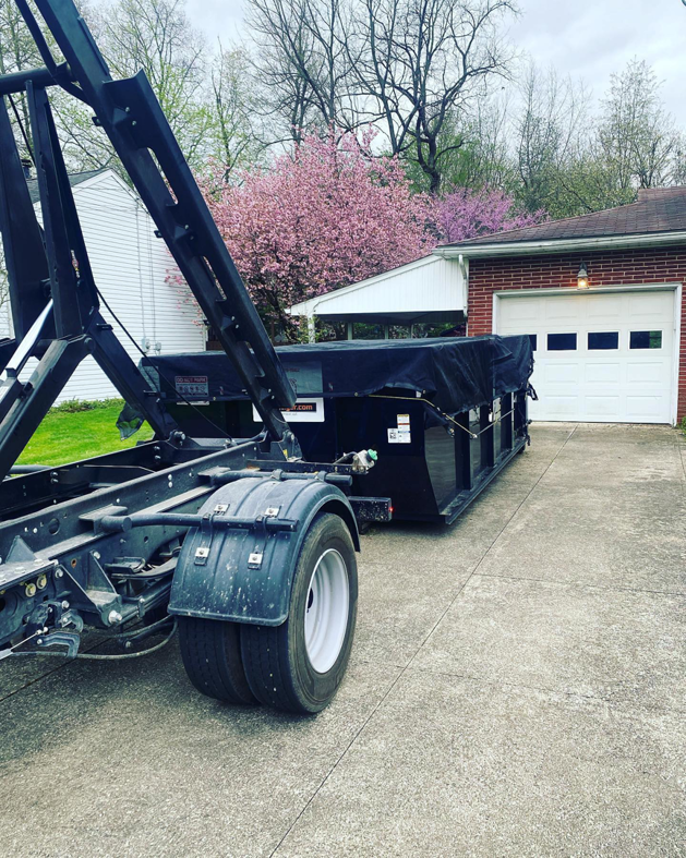 A trash_tiger truck transporting a covered roll-off dumpster in a residential driveway in Canton, OH.