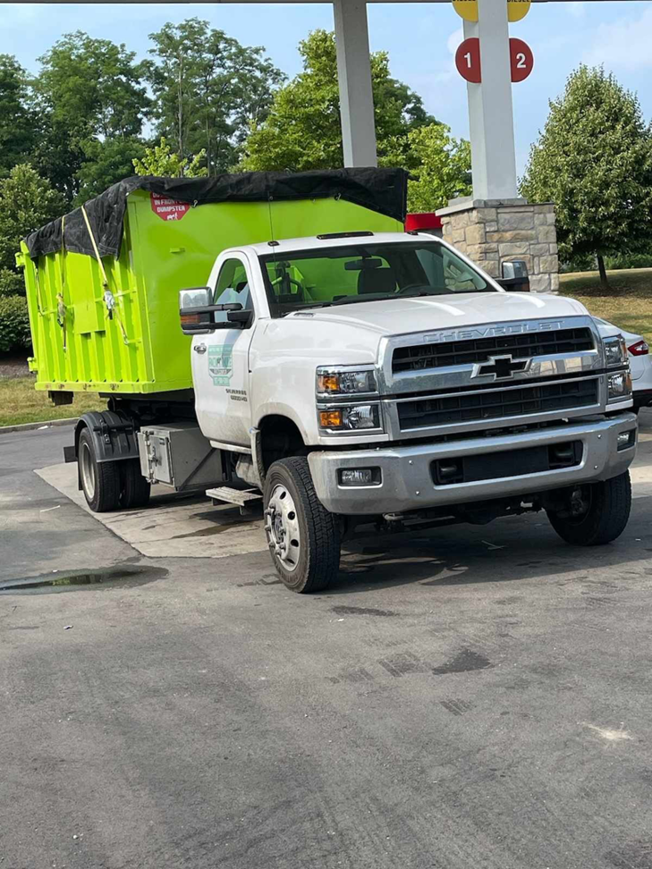 A Pack Mule Dumpsters Dayton, OH truck transporting a full, tarp-covered dumpster, ready for general junk removal.