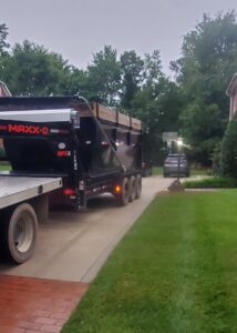 A white pickup truck transporting a full black dumpster trailer, completing a junk removal job for Standard Dumpster LLC in Rock Hill, SC.