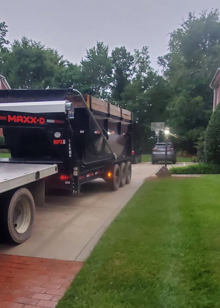 A white pickup truck transporting a full black dumpster trailer, completing a junk removal job for Standard Dumpster LLC in Rock Hill, SC.