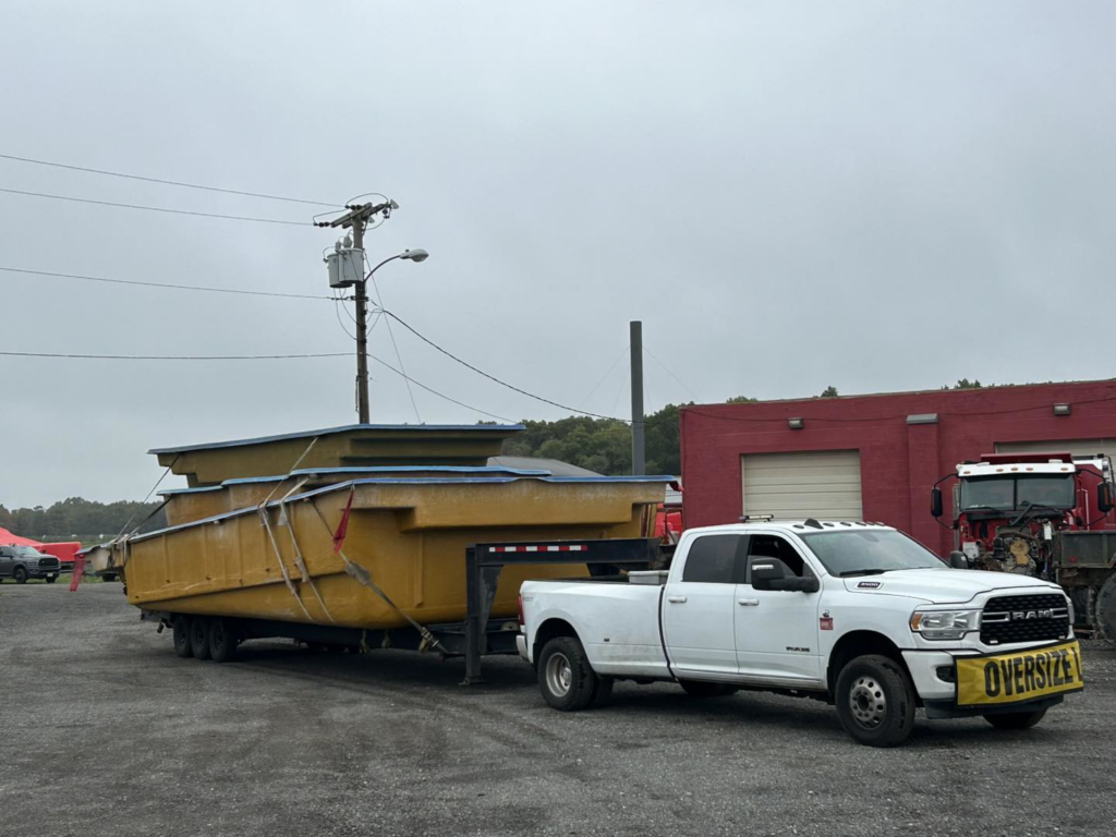An oversized truck transporting multiple yellow composite pool shells for Composite Pools USA in Newfield, NJ.
