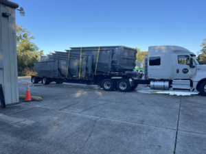 A semi-truck transporting multiple empty roll-off dumpsters for delivery at A-1 Roll-Off Rentals, LLC in Baton Rouge, LA.