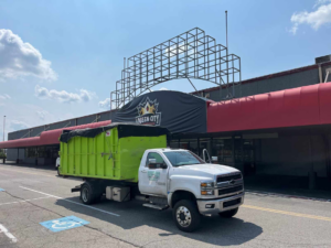A Pack Mule Dumpsters Dayton, OH truck with a covered dumpster parked at a commercial site for junk removal services.