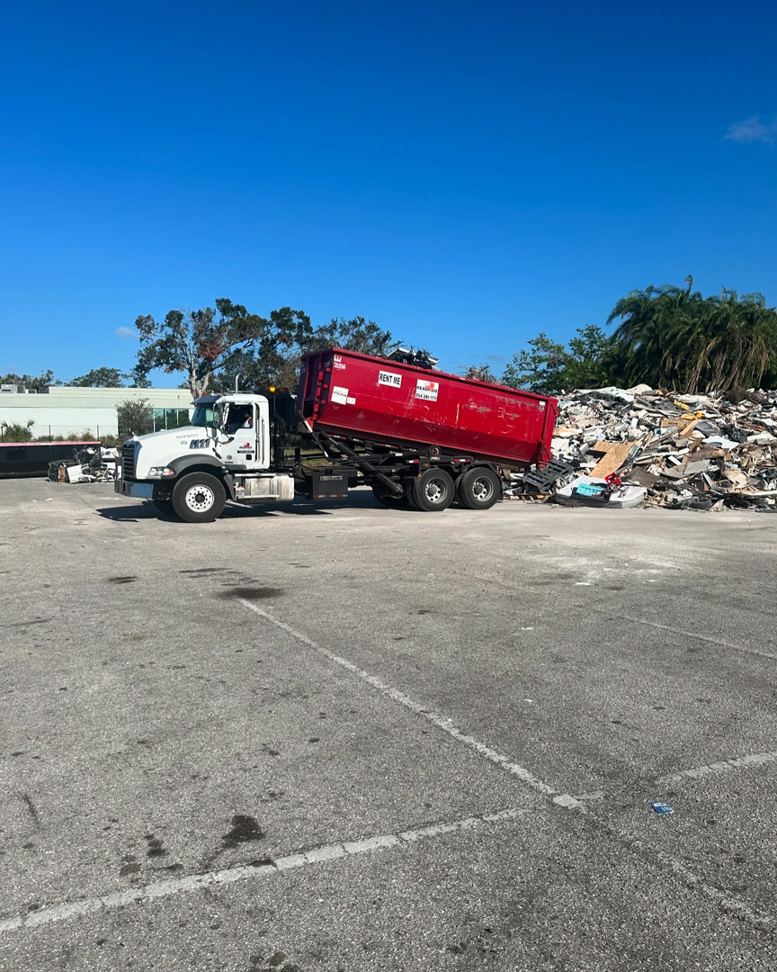A truck with a red dumpster positioned next to a large pile of general junk for removal by Dumpster Rental Florida in West Park, FL.