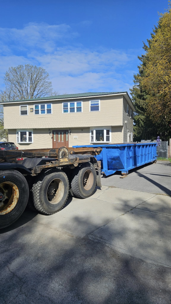 A Franklin's Disposal & Roll-Off Service truck parked with a blue roll-off dumpster in a residential driveway in Utica, NY.