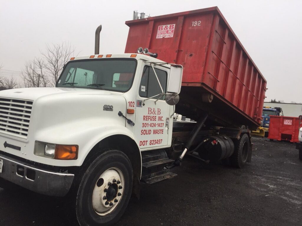 A white truck with a red roll-off dumpster, branded B & B Refuse Inc, for junk removal in Rockville, MD.