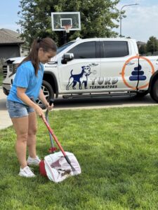 A Turd Terminators employee cleaning a backyard, scooping pet waste with a branded truck nearby in Omaha, NE.