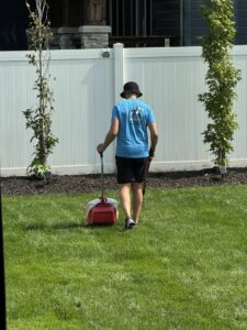 A Turd Terminators employee walking across a lawn with a pooper scooper, performing pet waste removal in Omaha, NE.