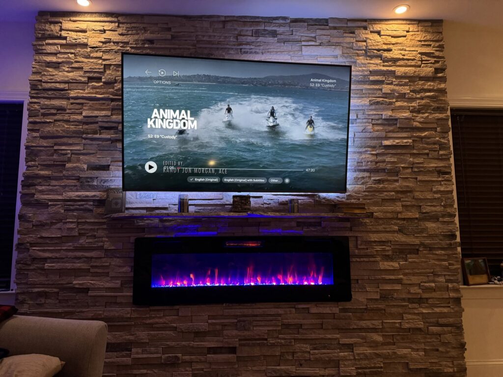 A mounted television and electric fireplace integrated into a custom stone veneer accent wall by JRG General Home Services, LLC in Toms River, NJ.