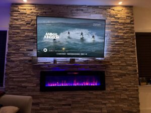 A mounted television and electric fireplace integrated into a custom stone veneer accent wall by JRG General Home Services, LLC in Toms River, NJ.