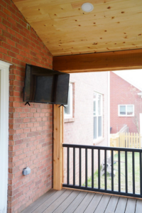 A television mounted on a brick wall of a newly built screened porch by Vision Construction in Framingham, MA.