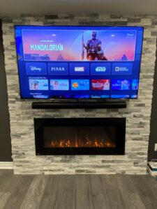 A wall-mounted TV and electric fireplace integrated into a stone veneer wall, installed by Dovetails Services LLC in Derry, NH.