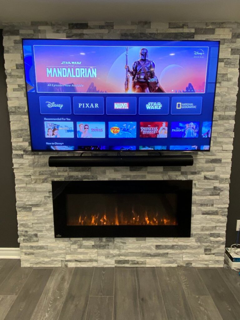 A wall-mounted TV and electric fireplace integrated into a stone veneer wall, installed by Dovetails Services LLC in Derry, NH.