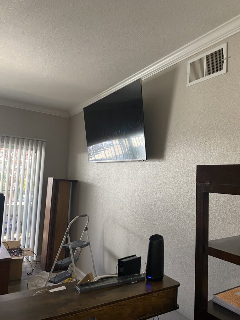 A large television professionally mounted on a wall, with a ladder nearby, installed by The Handy Nevadan LLC in Reno, NV.