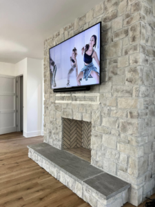 A flat-screen TV mounted above a stone fireplace with a herringbone tile insert by Coleman Builders in Mount Pleasant, SC