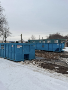 Two blue roll-off dumpsters from Ryan's Roll-Off Dumpsters placed in a snowy, muddy area in Owensboro, KY.