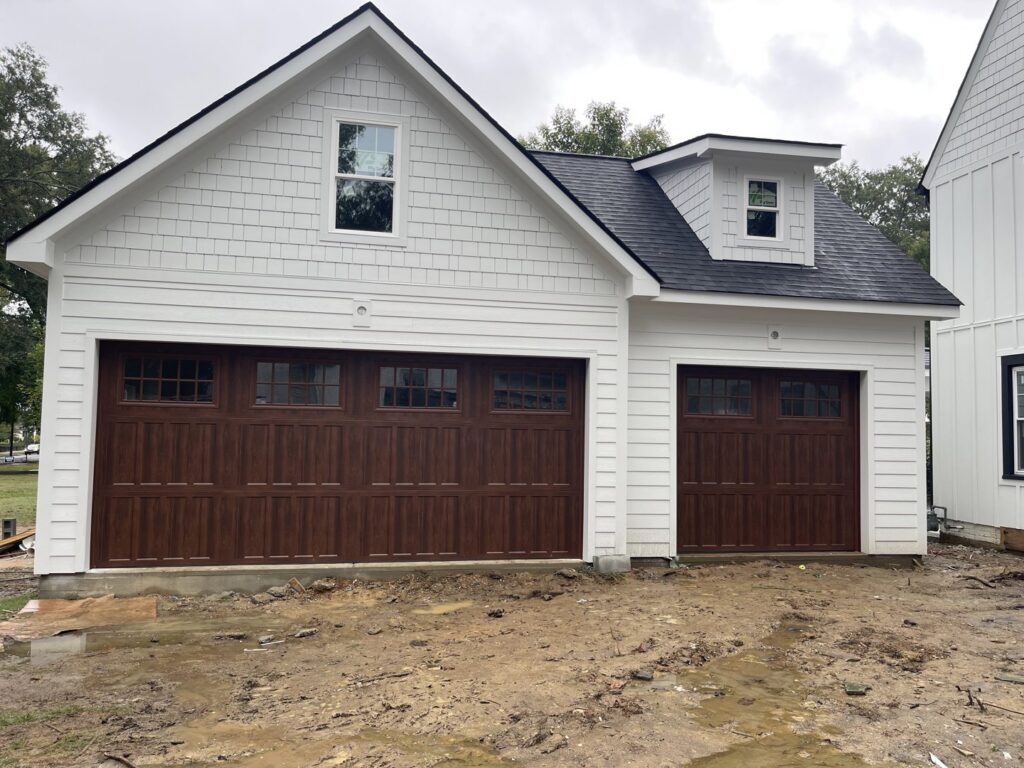 Two brown wooden-style garage doors installed on a white building by Total Garage Works in Indian Trail, NC.