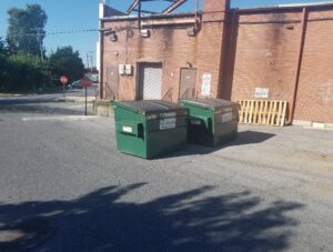 Two green commercial dumpsters from Total Waste placed outside a brick building in Baltimore, MD.