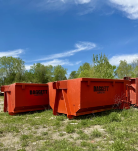 Two orange dumpsters from Daggett Container Service LLC, branded 'DAGGETT DUMPSTERS', in a field in Lansing, MI.