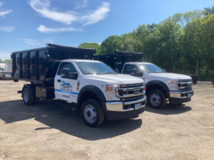 Two white Classic Disposal trucks with dumpsters on their beds, parked in Malden, MA, ready for junk removal services.