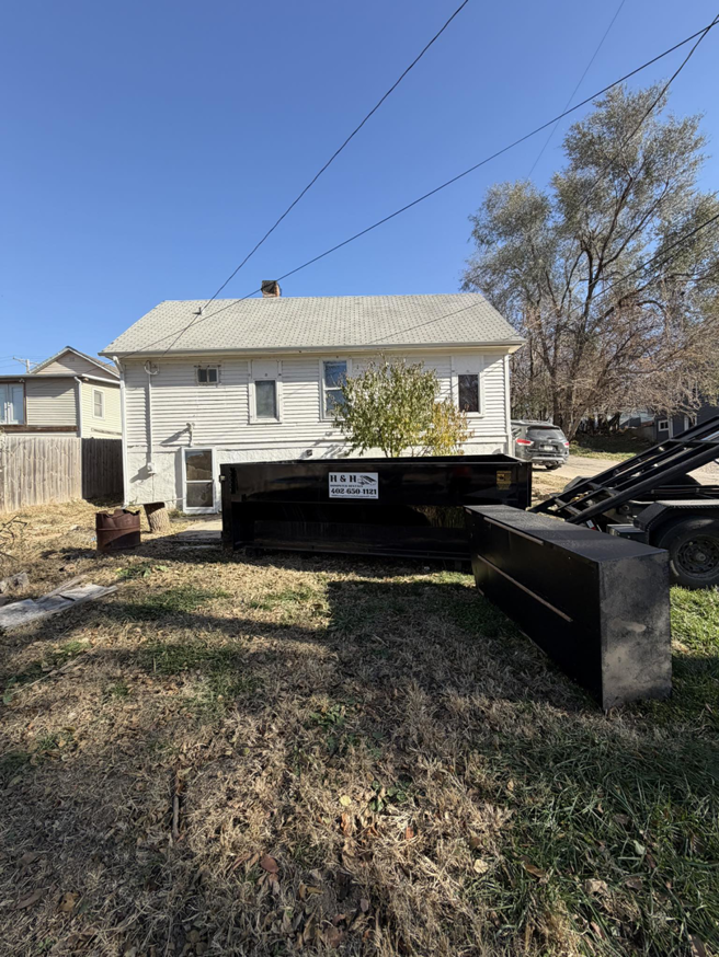 Two H & H Dumpster Rental dumpsters, one on a truck and one on the ground, in a residential backyard in Rootstown, OH.