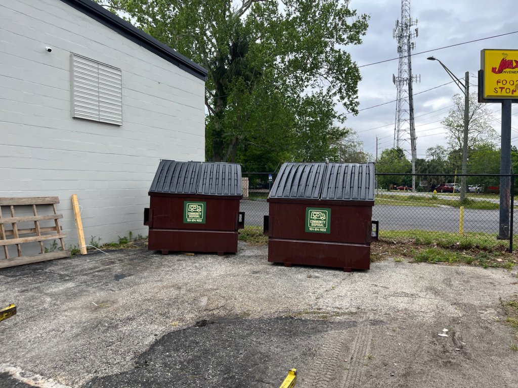 Two brown commercial dumpsters from Community Disposal positioned outside a building for junk removal in Jacksonville, FL.