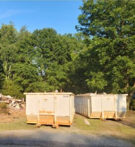 Two white dumpsters on a job site with a pile of debris in the background, provided by Standard Waste Enterprises in Greenville, SC.