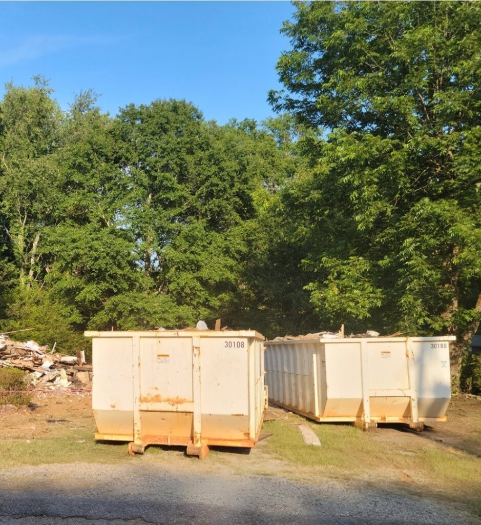 Two white dumpsters on a job site with a pile of debris in the background, provided by Standard Waste Enterprises in Greenville, SC.
