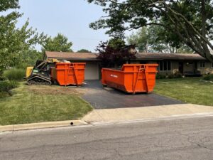 Two orange dumpsters and a small excavator on a residential driveway for junk removal by Lil Man W/A Can LLC in Columbus, OH.