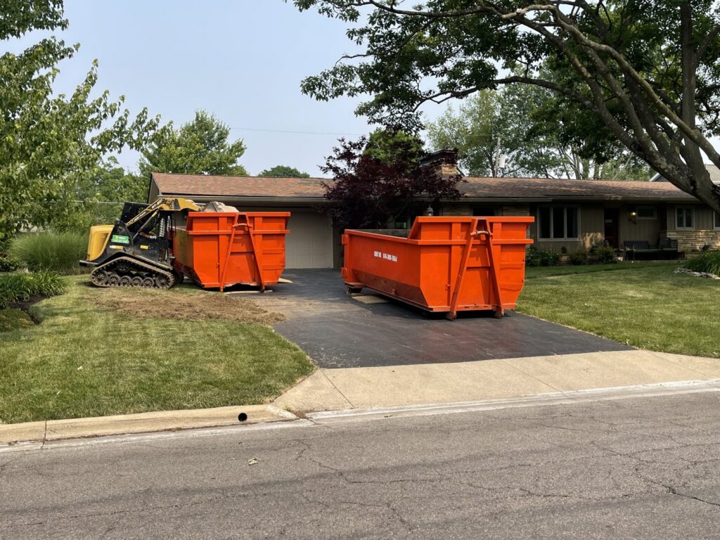 Two orange dumpsters and a small excavator on a residential driveway for junk removal by Lil Man W/A Can LLC in Columbus, OH.
