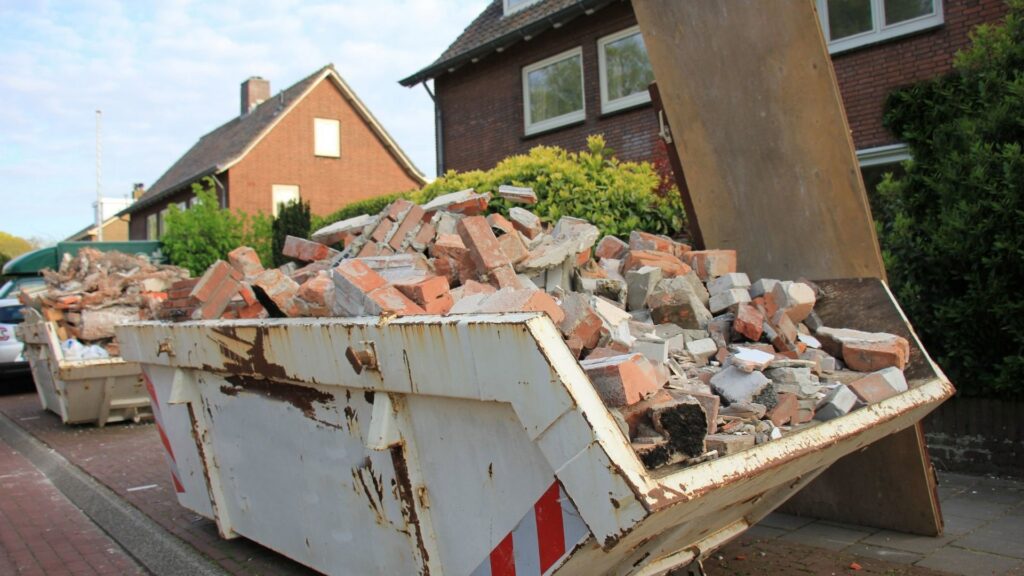 Two roll-off dumpsters, one filled with bricks and concrete debris, positioned near residential homes for junk removal in Sterling Heights, MI.