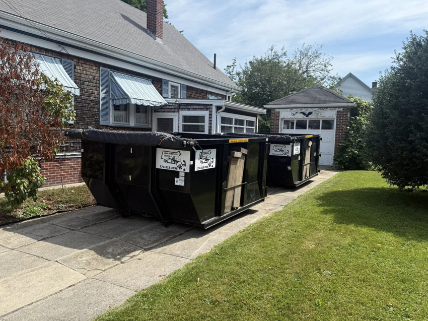 Two black dumpsters from Mini Dumpster Rentals placed on a residential driveway in New Bedford, MA.