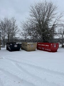 Two dumpsters, one tan and one red, from American Dumpster Rentals placed in front of a house with junk in Morrilton, AR.