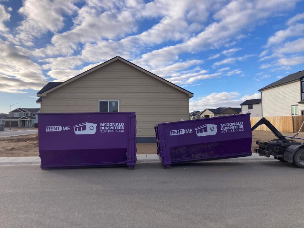 Two McDonald Dumpsters purple dumpsters being delivered or picked up on a residential street in Bar Nunn, WY.
