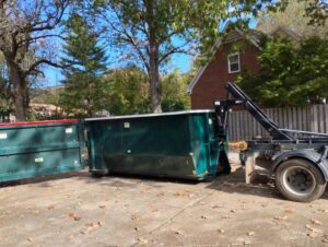 Two green dumpsters, one being loaded onto a truck, by Beetles Dumpsters Rental & Junk Removal in Huntsville, AL.
