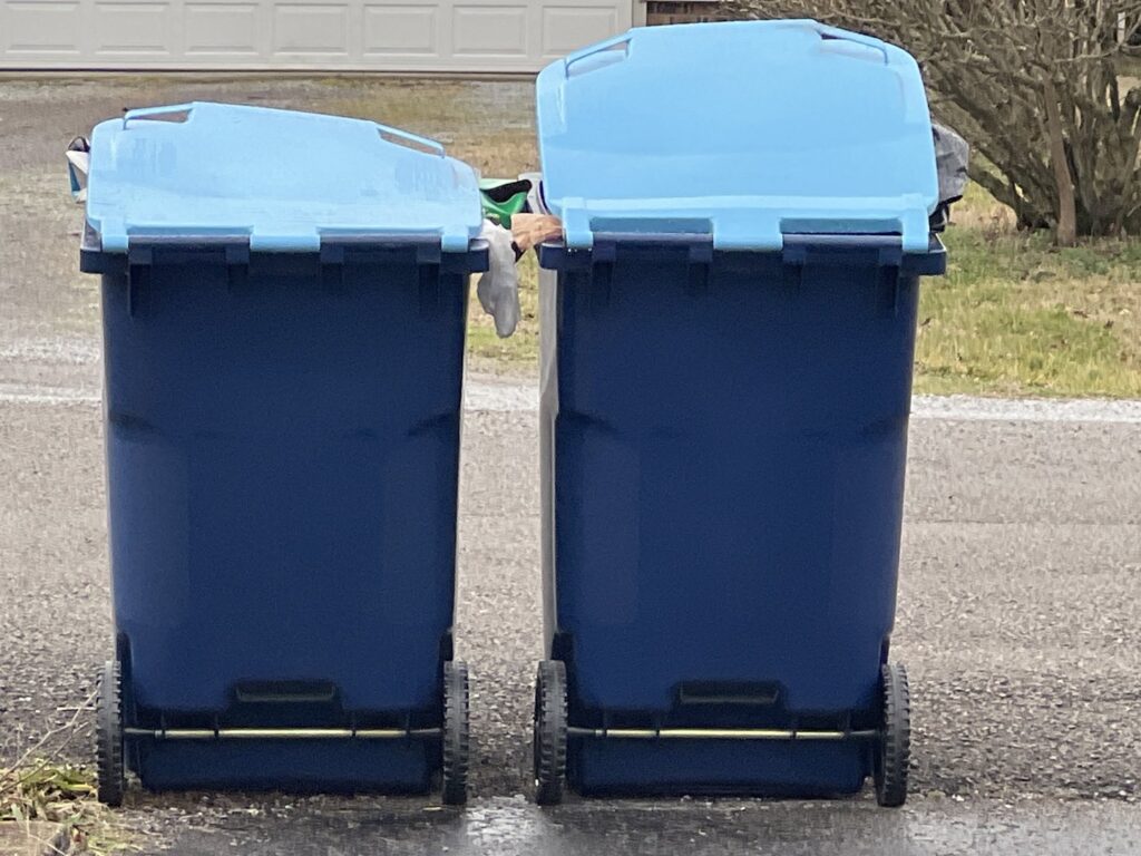 Two blue trash bins from One Waste Solutions, full of waste, placed on the roadside in Murfreesboro, TN, awaiting pickup.