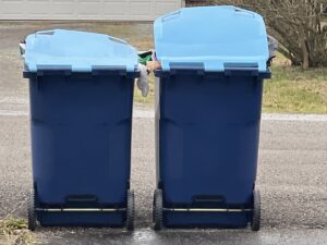 Two blue trash bins from One Waste Solutions, full of waste, placed on the roadside in Murfreesboro, TN, awaiting pickup.
