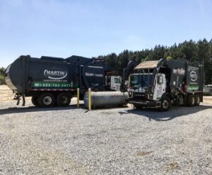 Two Martin Environmental garbage trucks parked side-by-side in a gravel lot in Dothan, AL.