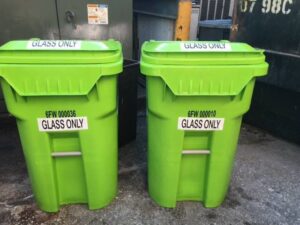 Two green recycling bins labeled 'Glass Only' from Fisher Recycling, placed in a service area in Charleston, SC.