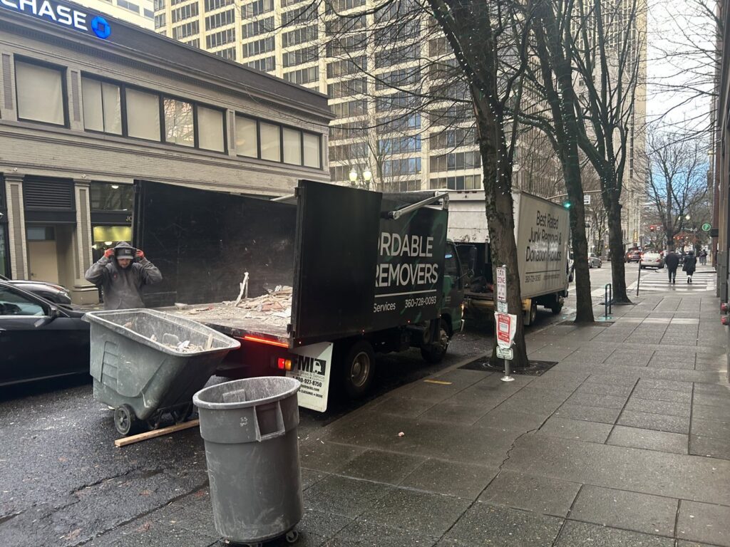 Two OnPoint Removal Services trucks, one with an open bed full of debris, parked on a city street during a junk removal job in Vancouver, WA.