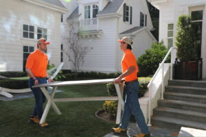 Two The Junkiez Junk Removal workers carrying a long table across a residential lawn in Los Angeles, CA.