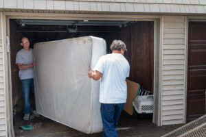 Two men carrying a large mattress out of a garage for A1 Junk Removal Of Tucson, AZ.