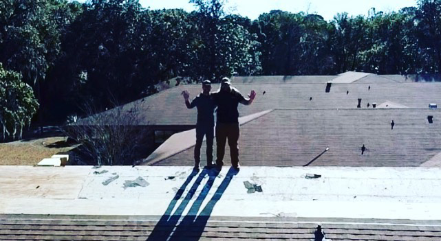Two men standing on a roof undergoing repair, showcasing work by Charleston Roofs & Windows in North Charleston, SC.