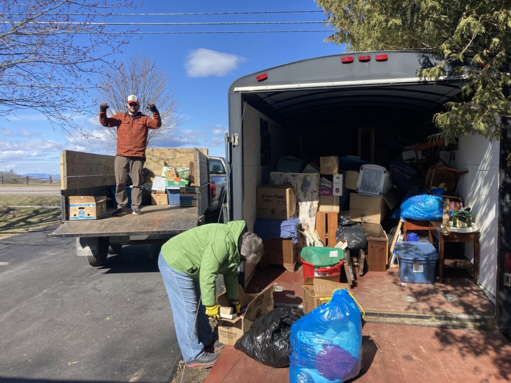Two people loading various junk items into an open trailer and truck bed for Hometown Hauling 802 in Milton, VT.