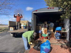 Two people loading various junk items into an open trailer and truck bed for Hometown Hauling 802 in Milton, VT.